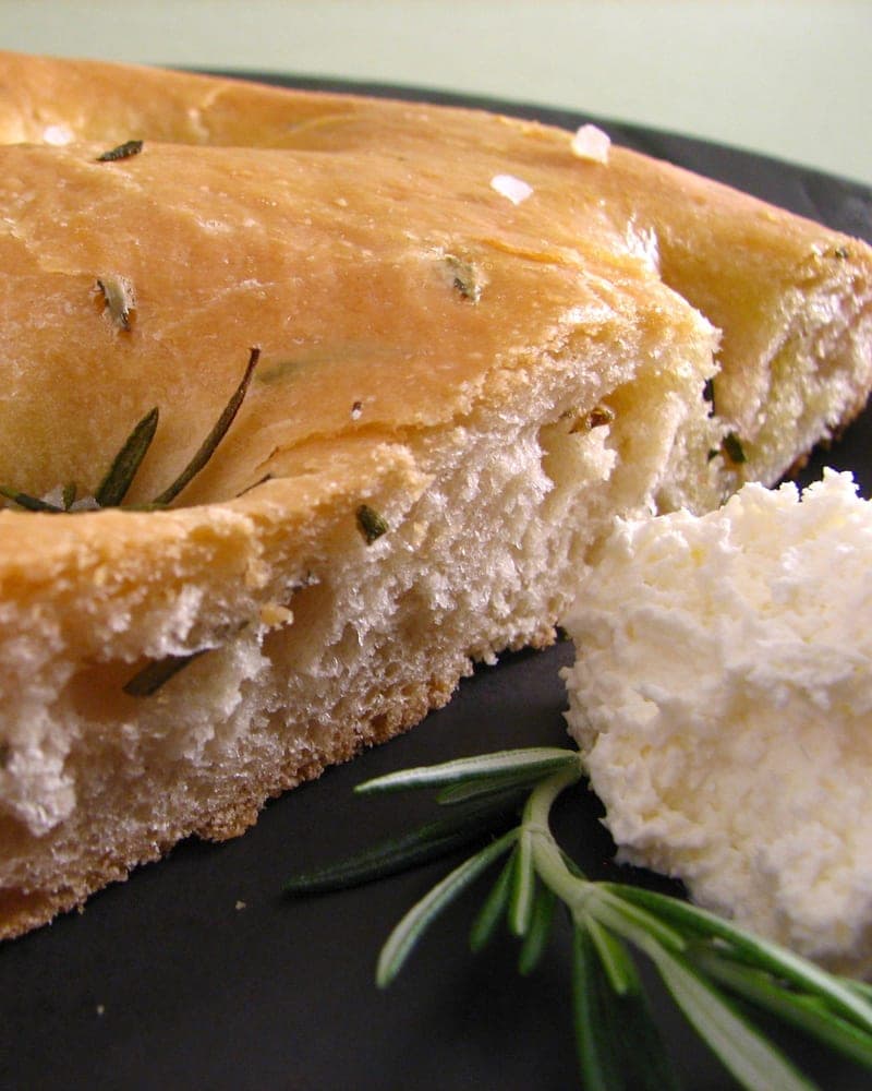 Torn focaccia studded with rosemary beside a wedge of soft cheese