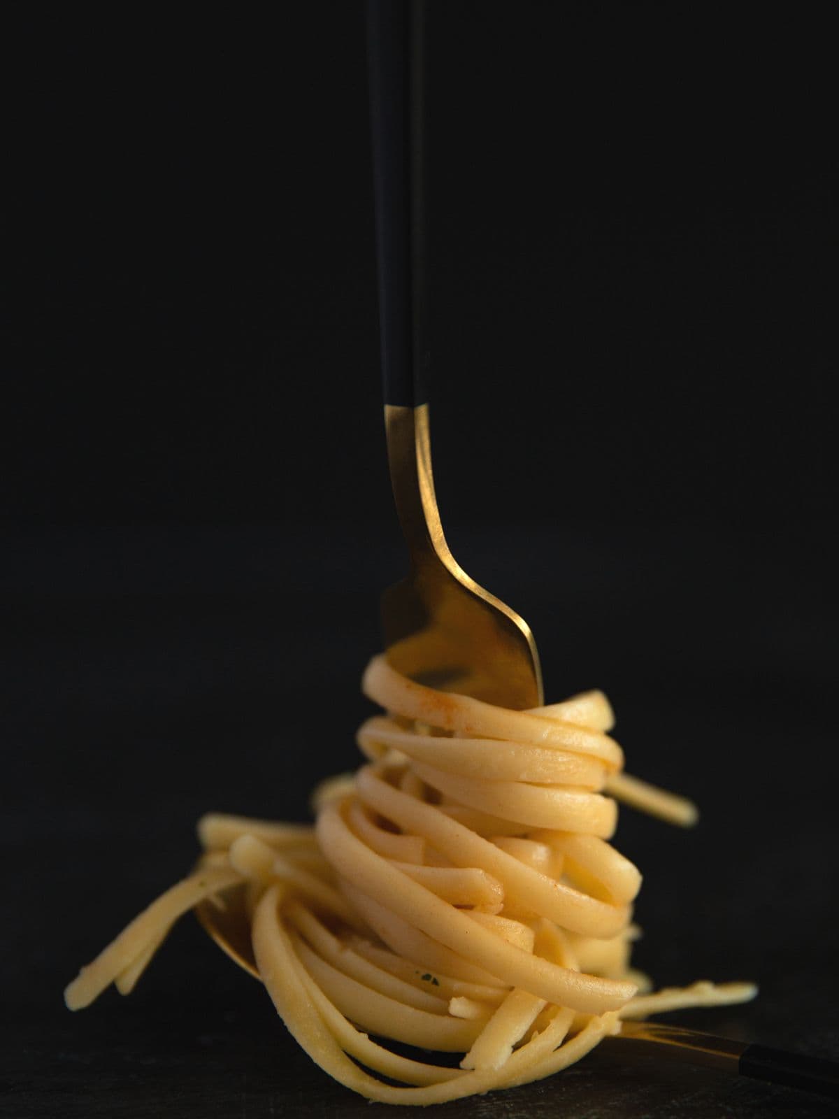 Pasta wound onto a brass fork, suspended against black