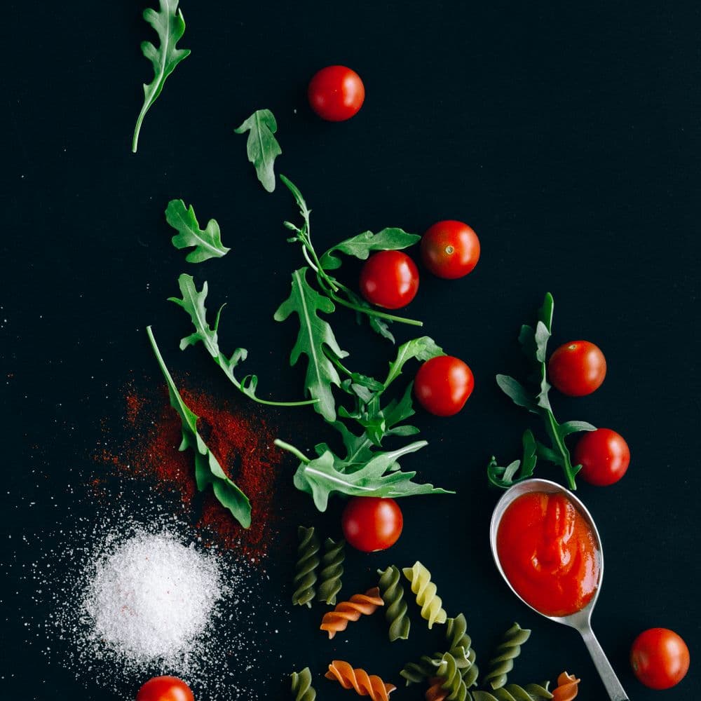 Tomatoes, arugula and dry pasta scattered across a dark surface