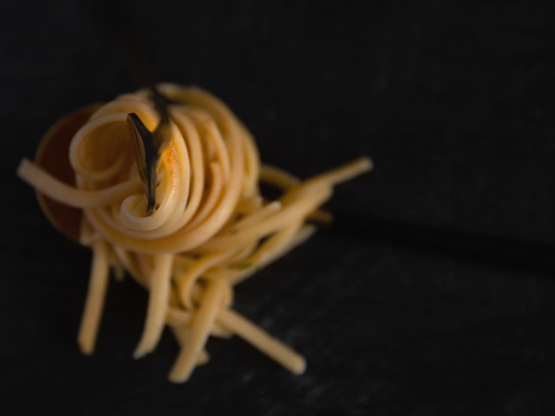A nest of fresh pasta lit from one side against deep shadow