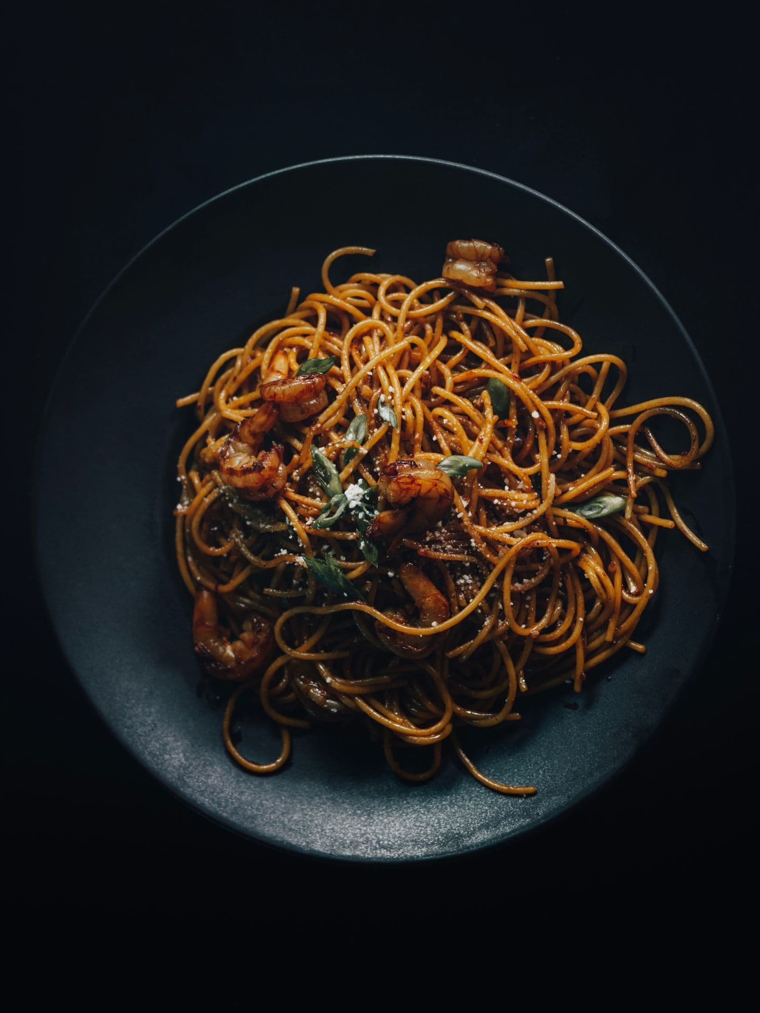 A dark nest of squid-ink pasta plated on black stoneware, lit from above