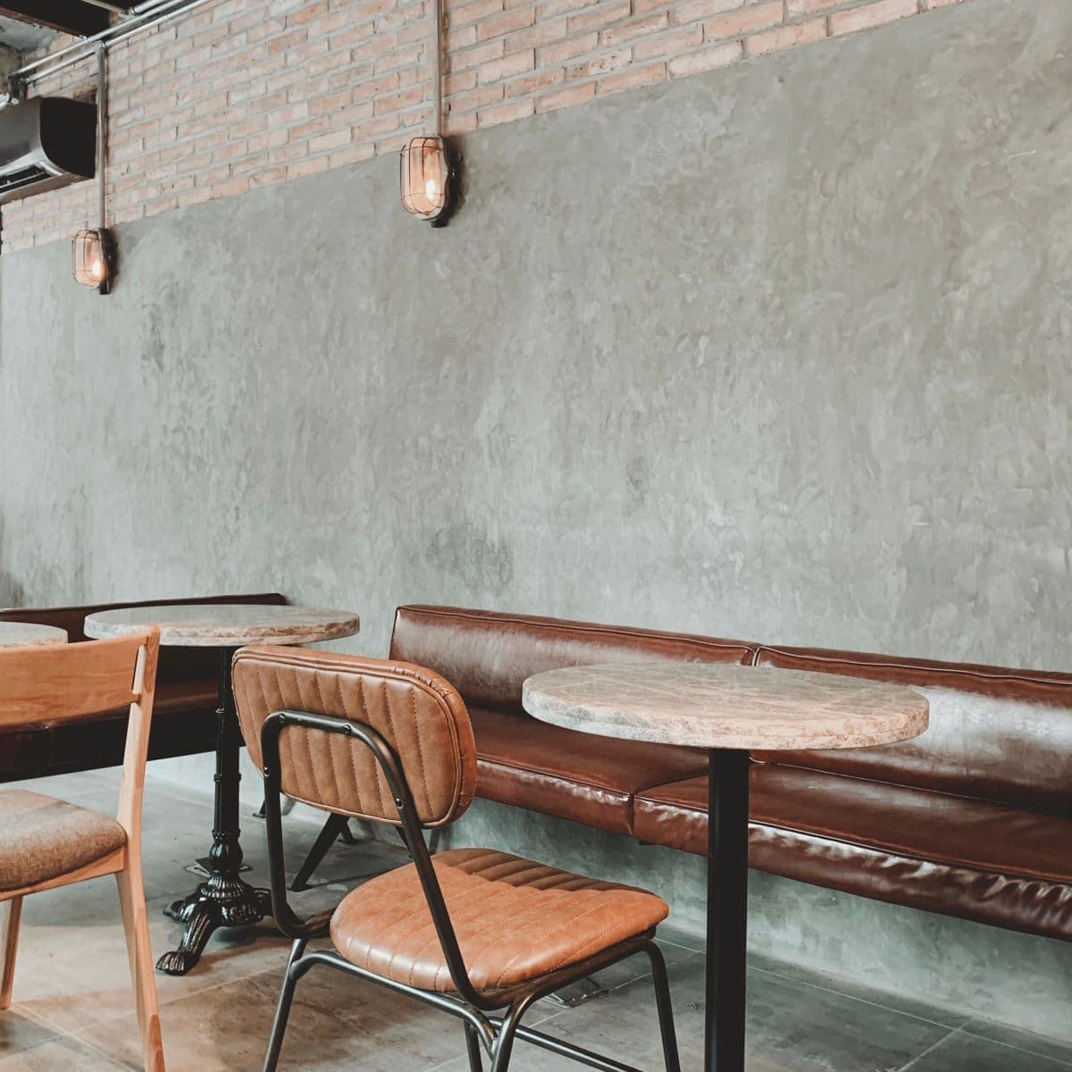 A banquette against a raw concrete wall with two bentwood chairs