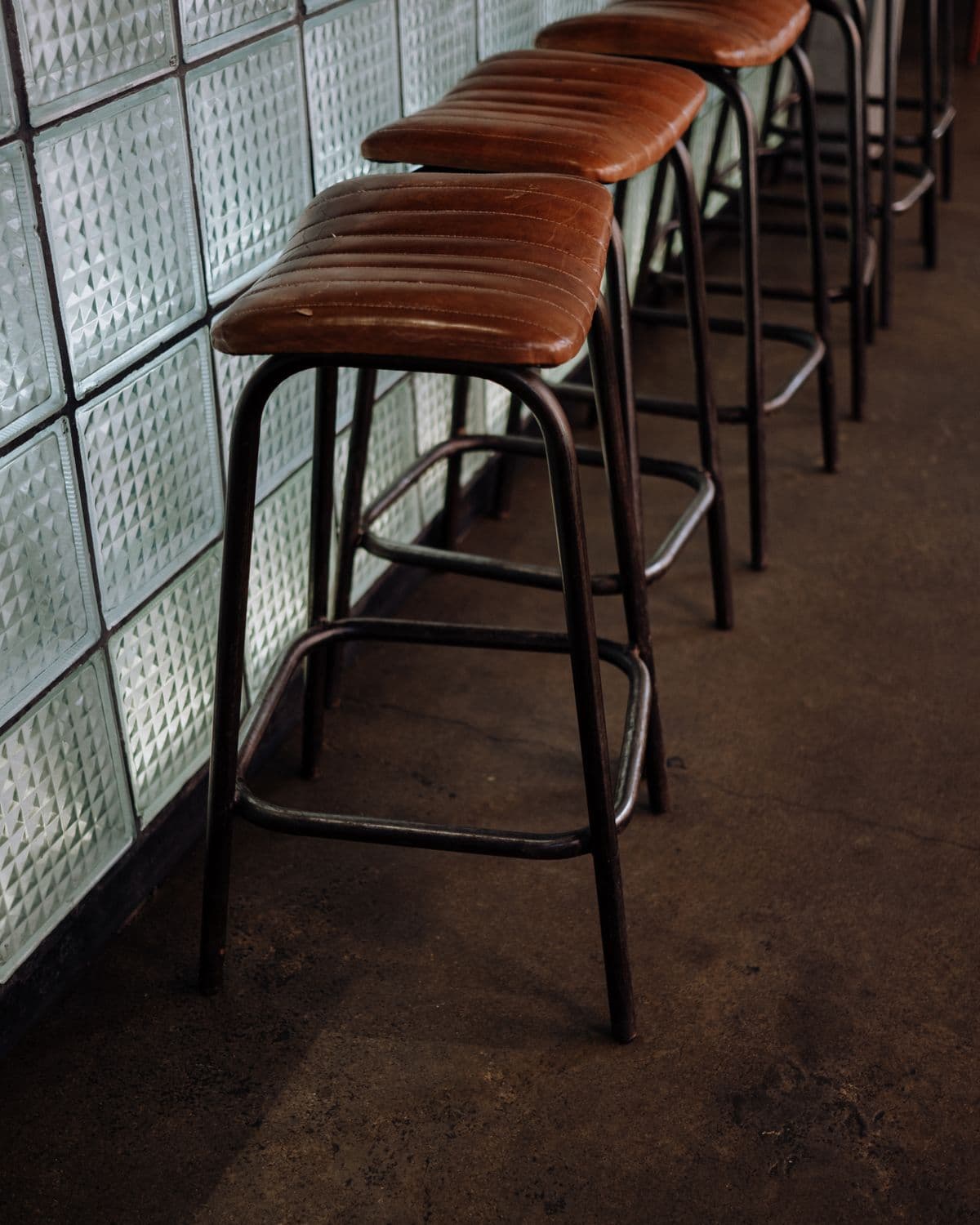 A row of leather stools along the pass, against a glass-block wall